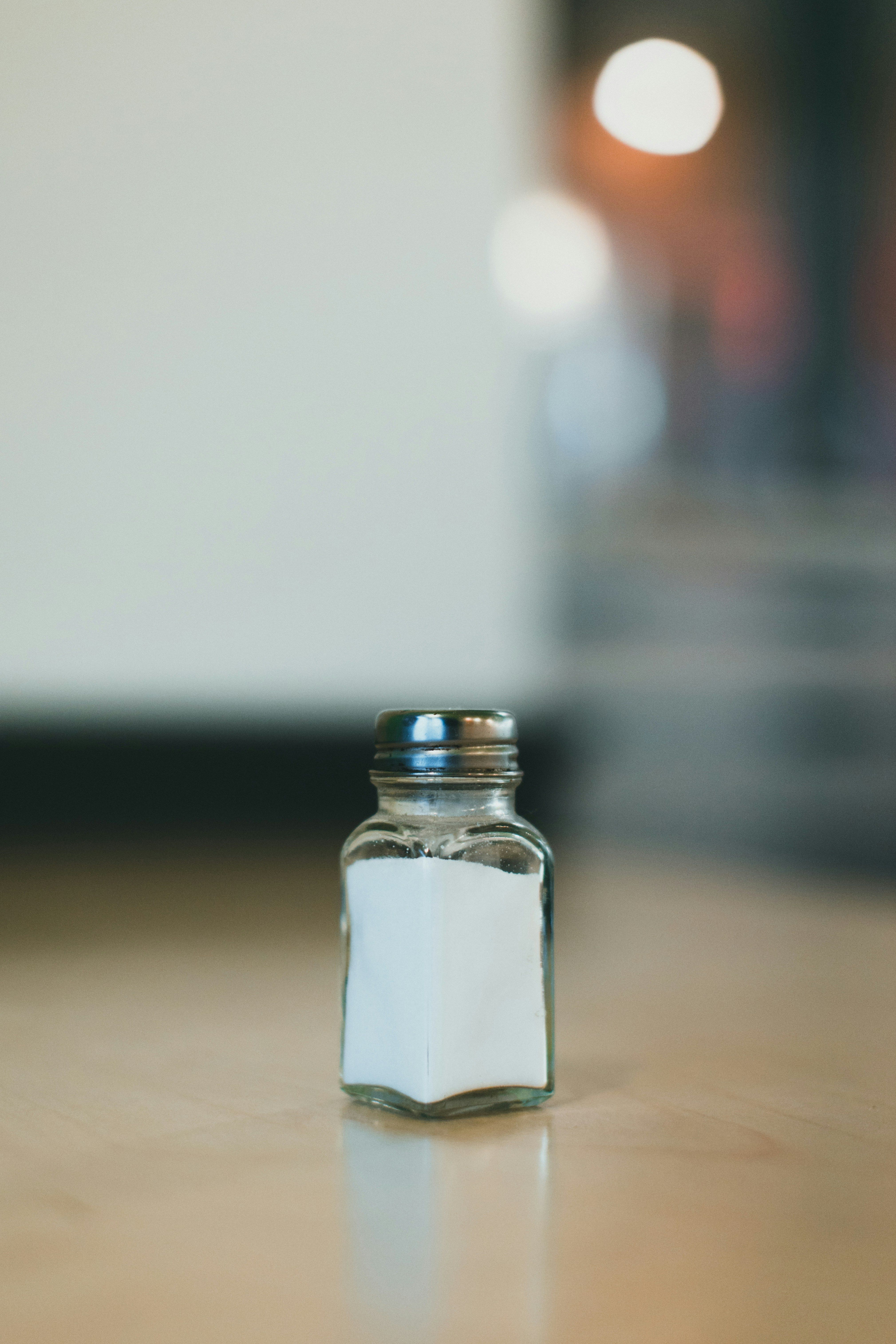 Small glass salt shaker filled with white salt on a wooden surface.