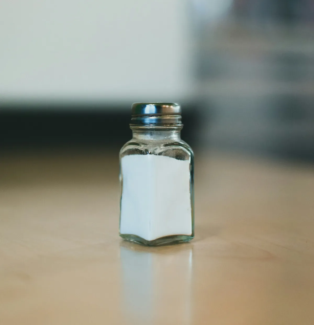 Small glass salt shaker filled with white salt on a wooden surface.